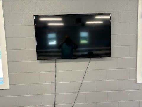A large flat-screen television mounted on the painted cinder-block wall of the Post 206 event room